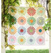 Colorful quilt with sunburst patterns hanging outdoors among tree branches.