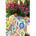 Colorful patchwork quilt draped over a bench in a garden of pink flowers.
