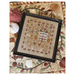 The finished Enchanted Autumn Sampler finished, framed, and staged on a fall quilt with pumpkin decor.