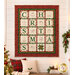 The completed C is for Christmas quilt, colored in red, green, and cream fabrics from the Christmastime collection by Maywood Studio, staged on a cream shiplap wall in a cozy living room filled with Christmas décor.