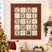 The completed C is for Christmas quilt, colored in red, green, and cream fabrics from the Christmastime collection by Maywood Studio, staged on a cream shiplap wall in a cozy living room filled with Christmas décor.
