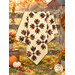 The completed Bear Hugs quilt, colored in warm flannels from the Flannel Season collection by Moda Fabrics, artfully draped over a rustic wood farm fence with a barn in the background and pumpkins and florals in the foreground.