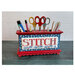 Decorated organizer holding scissors, pens, and craft tools, embellished with a finished cross stitch project that says "Stitch."