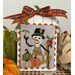 Cross-stitch snowman decoration with autumn bow and pumpkins on a festive display.
