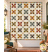 The completed Harrisonburg Quilt,  colored in rich fabrics from the Jamestown collection from Andover Fabrics, staged on a white porch wall with coordinating décor and furniture.