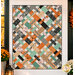 The completed Picnic Quilt Kit, colored in gray, mint green, white, pink, and orange fabrics from the Frank and Friends collection by Riley Blake Designs, hung on a white shiplap porch wall beside coordinating florals.