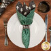A top down shot of the napkin with the mint spiderweb fabric facing out, staged on a coordinating table setting on a warm wood table.
