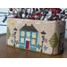 Cross-stitch house scene on a fabric box with lamps, trees, and flowers.