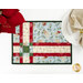 A top down close up of one of the Fat Quarter Shuffle Mats, demonstrating the Christmas fabric prints and colors; flowers and a plate with a napkin peek into frame.