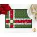 A top down close up of one of the Fat Quarter Shuffle Mats, demonstrating the Christmas fabric prints and colors; flowers and a plate with a napkin peek into frame.