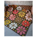 an image of the Knitted Blooms quilt finished and staged on a leather couch in a concrete room.