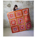 An image of a woman holding the finished granny patch quilt done in brown, pink, purple, and blue fabrics, with a concrete backdrop