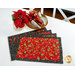 The four completed Self-Binding Placemats, fanned out and  colored in red, cream, and black fabrics from the Poinsettia Radiance collection from White Owl Textiles, staged on a white table with coordinating décor.