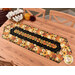 The completed Easy Striped Table Runner, colored in warm, autumn themed prints from the Give Thanks collection by Timeless Treasures Fabrics, staged on a warm wooden table with coordinating décor and table settings.