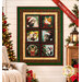The Merry Cats Panel Quilt Kit, colored in black, red, and green fabrics from the Merry Cats collection by Benartex, hung on a cream shiplap wall and staged with coordinating furniture and décor; a small cat sleeps on a white couch.