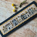 A cross stitch village with whimsical houses surrounded by bees, beehives, sunflowers, and honey-inspired details.