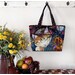 The completed tote made with a colorful cat-themed panel, staged against a wall with coordinating flowers.