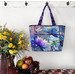 The completed tote made with a colorful floral and dragonfly-themed panel, staged against a wall with coordinating flowers.