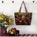 The completed tote made with a colorful campfire-themed panel, staged against a wall with coordinating flowers.