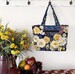 The completed tote made with a colorful floral-themed panel, staged against a wall with coordinating flowers.