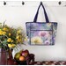 The completed tote made with a colorful floral-themed panel, staged against a wall with coordinating flowers.