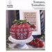 Red tomato-shaped stitched sampler on a pedestal with small tomatoes and a chart in the background.