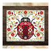The finished Ladybug Love cross stitch project featuring a stylized ladybug surrounded by red and orange florals, framed with a dark wood border.