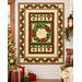 The completed Ribbon Border Panel Quilt, colored in cream, red, and green fabrics from the Deck the Halls collection by Northcott Fabrics, hung on a white shiplap wall in a cozy living room with coordinating décor.