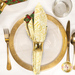 A top down shot of the napkin with the cream and gold fabric facing out, staged on a coordinating gold table setting on a white marble table.