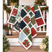 The completed Presently quilt, colored in red, green, navy, light blue, cream, and white fabrics from the When Snow Falls collection from Moda Fabrics, artfully draped over a white porch fence and staged with coordinating greenery and décor.
