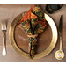 A top down shot of the napkin with the multicolor paisley fabric facing out, staged on a coordinating gold table setting on a white table.