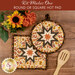 The completed Folded Hot Star Pads colored in autumn fabrics from the Bountiful collection by Riley Blake Designs, staged on a wooden table with coordinating décor.