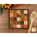 The completed Fusible Grid Hot Pad colored in autumn fabrics from the Bountiful collection by Riley Blake Designs, staged on a wooden surface with a wooden spoon.
