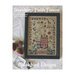 Front cover of the Strawberry Fields Forever cross stitch pattern finished in a black frame next to stitched strawberry pincushions and buttons.