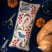 The finished pillow with three birds amongst berries and leaves, staged amongst a pair of scissors, felt pumpkins, and a wooden bird.