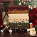 A stack of the fabrics included in the A Vintage Christmas II collection, with a christmas tree and a lantern and a poinsettia and ornaments and thread and ribbon.