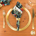 A top down shot of the napkin with the dark teal blue fabric facing out, staged on a coordinating gold table setting on a white table.
