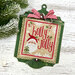 Green wooden ornament display with a mounted cross stitch design reading "Holly Jolly," with Santa, evergreen trees, snowflakes, and a red-and-white striped bow.