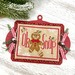 A Christmas cross stitch ornament with a gingerbread man, red bow, and candy cane-inspired lettering.
