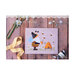 Front cover of The Gnome and the Bees cross stitch pattern showing the finished pattern laid on a wooden plank table next to florals, ribbons, and buttons.