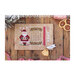 Front cover of the Santa's Advent Calendar cross stitch pattern showing the finished pattern laid on a wooden plank table next to ribbon, shortbread cookies, and a pine bough.