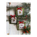 Alternative stamp cross stitch designs hung on pine branches against a white plank background.