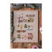 Front cover of the Christmas in the City cross stitch pattern showing the finished pattern laid on a wooden plank table on top of pine boughs, string, and Christmas gift tags.
