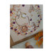Photo of the finished Snack in the Woods cross stitch pattern placed on a floral fabric board next to pumpkins, cookies, and maple leaves.