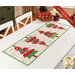 The completed Crazy Christmas Tree table runner, colored in bright red, green, and white fabrics from the Snow Time collection by Moda Fabrics, staged on a white table with coordinating napkins and décor.