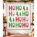 The completed Jollity quilt kit, colored in bright red, green, and white fabrics from the Snow Time collection by Moda Fabrics, staged on a white paneled wall and surrounded by coordinating garlands, presents, and décor.