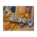 Photo of the four finished Happy Halloween Flag patterns strung on a wooden desk next to jack-o'-lanterns and fall leaves.