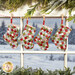 The four completed Fast Fusible Patchwork Stockings colored in wintry prints from the Chilly collection by Moda Fabrics, hung on a striped string by clothespins in a window that looks over a snowy scene; Christmas garlands peek into frame from the top and bottom.