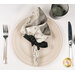 A top down shot of the napkin with the white floral fabric facing out, staged on a complementary cream table setting on a white table.
