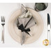 A top down shot of the napkin with the gray dotted fabric facing out, staged on a complementary cream table setting on a white table.